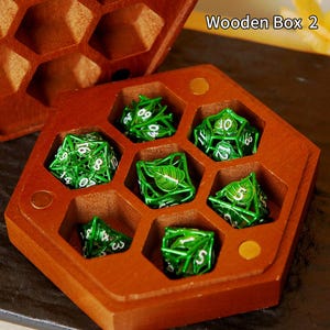 May include: A hexagonal wooden box in reddish-brown, containing seven green dice with white numerals. The dice feature a leaf design. The text "Wooden Box 2" is visible. The box is designed to hold the dice.
