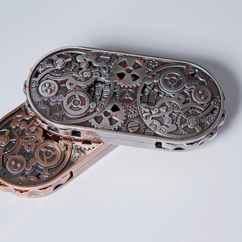 May include: Two steampunk-style metal cases with intricate gear designs. One case is silver with red accents, and the other is bronze. The cases are oval-shaped and feature detailed mechanical components.