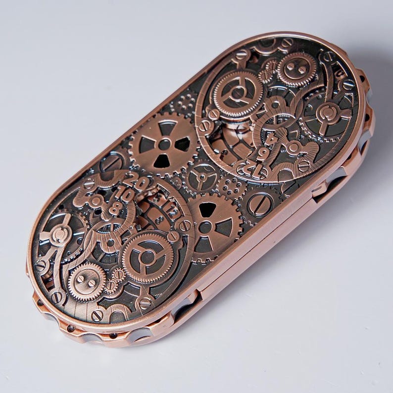 May include: A steampunk-style, copper-colored metal case with intricate gear and cog designs. The rectangular case features a detailed arrangement of various-sized gears, creating a mechanical aesthetic. The case has a hinged design and a metallic finish.
