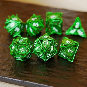May include: A set of seven green metal dice with white numbering. The dice are in various geometric shapes, including a d4, d6, d8, d10, d12, and d20. The dice have a leaf-like design.