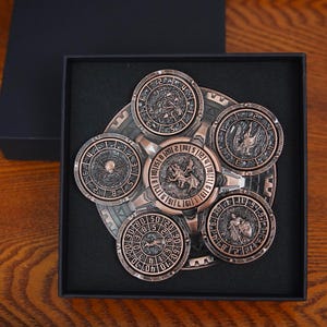 May include: A copper-coloured metal fidget spinner featuring a central circular piece with a dragon relief and five surrounding circular discs, each displaying unique embossed figures and numerical markings, all housed in a black square gift box.