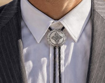 Könnte beinhalten: Eine silberne Bolo-Krawatte mit einem dekorativen floralen Design. Die Bolo-Krawatte wird mit einem weißen Hemd mit Kragen und einer grauen Nadelstreifen-Anzugjacke getragen. Das schwarze Band hängt vom silbernen Anhänger herunter.