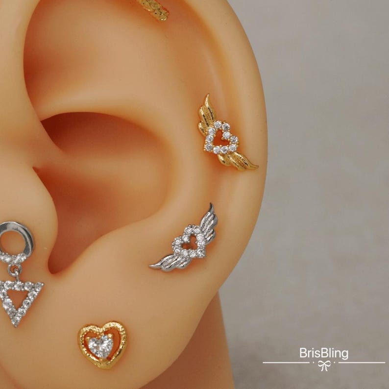Puede incluir: Tres pendientes de coraz&oacute;n de oro y plata con detalles de cristal. Los pendientes tienen forma de coraz&oacute;n con alas. Los pendientes son para piercings de cart&iacute;lago.