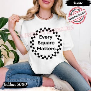 May include: White t-shirt with the text "Every Square Matters" inside a black and white checkered circle. The shirt is a Gildan 5000. The design is an original design.