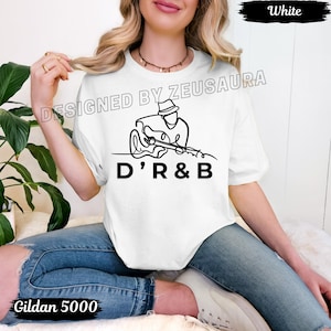 May include: White t-shirt with a black line drawing of a musician playing a guitar, with the text "D'R&B" below. The shirt also features the text "DESIGNED BY ZEUSAURA" and "Gildan 5000".