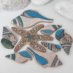 May include: A collection of ceramic sea life figurines, including seashells and a starfish. The figurines are painted in shades of blue, green, and brown, with white and tan accents. The starfish has a detailed design.