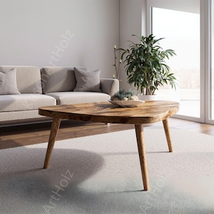 Puede incluir: Una mesa de centro de madera con una forma orgánica inusual. La mesa tiene un acabado marrón claro y tres patas anguladas. La mesa está colocada en un salón con un sofá beige, cojines y una planta grande.