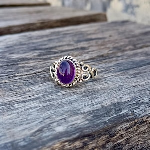 Op de afbeelding: Een zilveren ring met een ovale amethist-edelsteen gezet in een decoratieve zilveren band.