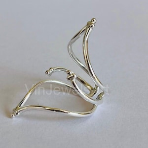 Peut inclure: Une manchette d'oreille en argent avec un design incurvé et ouvert. La manchette est composée de trois fils entrelacés.