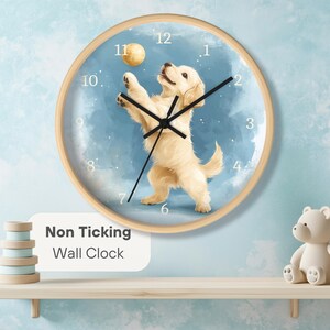 May include: Round wall clock with a light wood frame. The clock face features a playful illustration of a golden retriever puppy reaching for a ball against a blue background. The text "Non Ticking Wall Clock" is displayed.