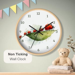 May include: Round wall clock with a light wood frame. The clock face features a watercolor painting of ladybugs on a green leaf. The text "Non Ticking Wall Clock" is on the lower left. The clock hands are black.