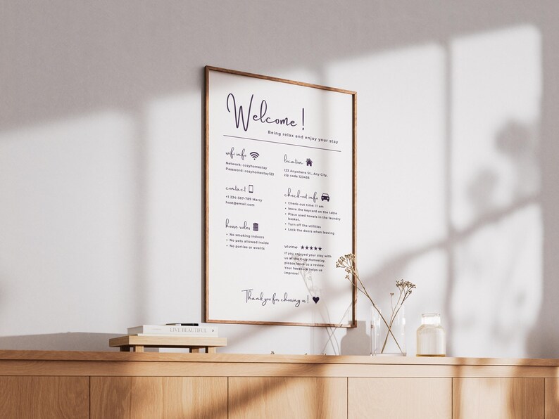 May include: A framed welcome sign with a wooden frame, featuring handwritten text in dark blue. The sign includes information about Wi-Fi, contact details, house rules, and check-out instructions. The sign is displayed on a wooden cabinet.