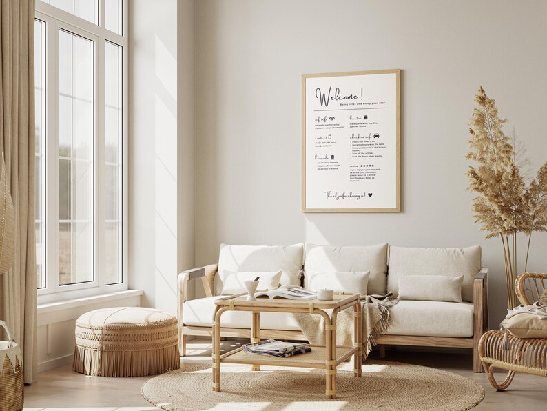 May include: A light-filled living room with a neutral color palette. A framed sign with the word "Welcome" hangs above a cream-colored sofa. A round jute rug, a woven ottoman, and a bamboo coffee table complete the cozy, inviting space.