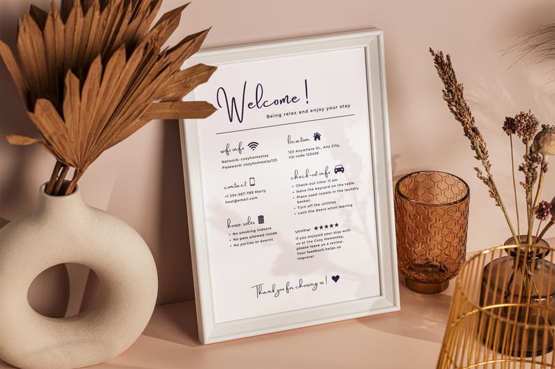 Framed welcome sign on a beige table with rustic vases, dried flowers, and a brown textured glass, conveying a warm and inviting atmosphere.