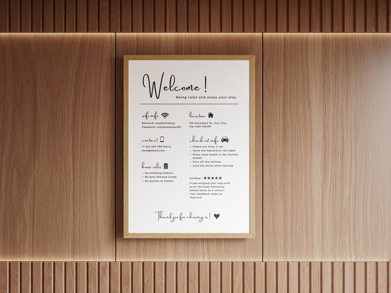 Framed "Welcome" info sign on a wooden wall. Details Wi-Fi, contact, location, house rules, check-out process, and review request. Warm, inviting tone.