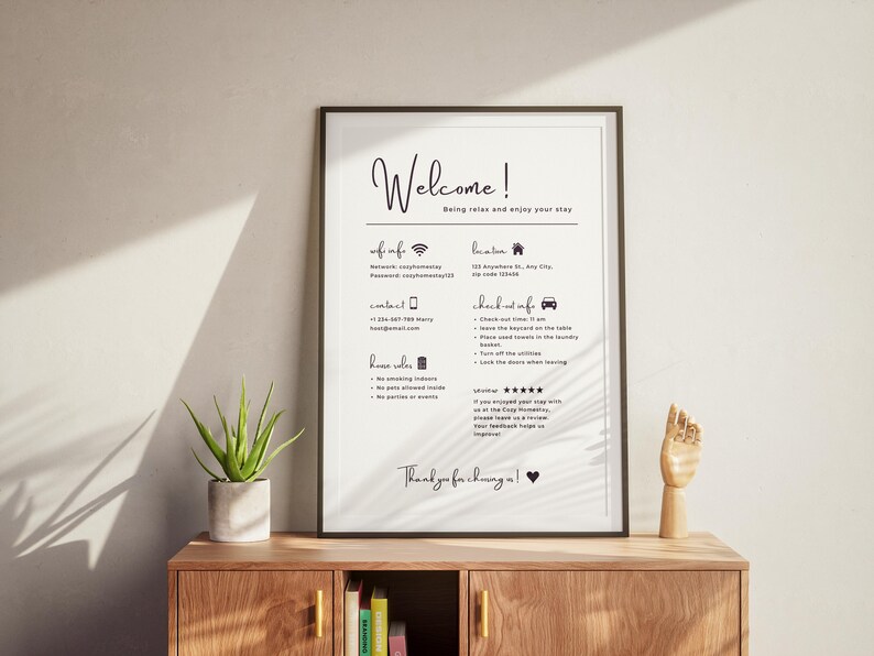 Framed welcome sign on a wooden shelf details Wi-Fi info, location, contact, and house rules. Nearby are a potted plant and a wooden hand model. Warm, inviting tone.