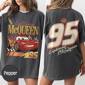 May include: Pepper-colored t-shirt featuring Lightning McQueen from the Cars movie. The front displays the character and text, while the back shows a large "95" and the character's name. The shirt has a vintage, distressed look.