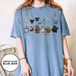 May include: Blue jean coloured t-shirt featuring Star Wars characters with Mickey Mouse-shaped balloons. The graphic includes R2-D2, a Stormtrooper, Chewbacca, BB-8, Grogu, and Darth Vader. The shirt also has the text "COMFORT COLORS BLUE JEAN".