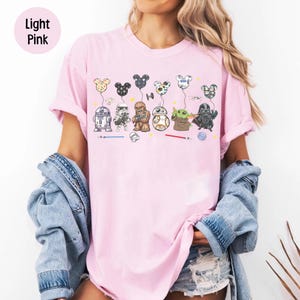 May include: Pale pink t-shirt with a Star Wars design. The graphic features characters and Mickey Mouse-shaped balloons. The text "Light Pink" is in a light pink circle in the upper left corner.