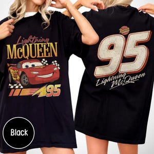 May include: Black t-shirt featuring Lightning McQueen from the Cars movie. The front graphic shows McQueen with the number 95, while the back displays a large number 95 and the Lightning McQueen logo. The shirt has a vintage, distressed look.