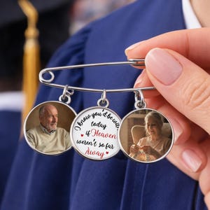 May include: A silver safety pin with three circular pendants. Two pendants feature photos of people, and the center pendant has the text "I know you'd be with today if Heaven weren't so far Away."