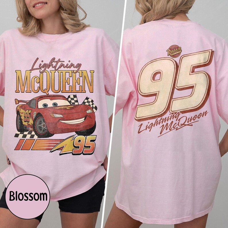 May include: A light pink t-shirt featuring Lightning McQueen from the Cars movie. The front of the shirt displays the character with the text "Lightning McQueen" and "95". The back of the shirt has a large "95" and "Lightning McQueen" text.