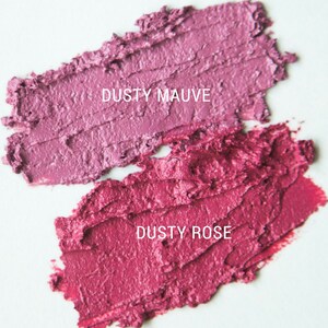 K&ouml;nnte beinhalten: Zwei Lippenstift-Farbmuster auf wei&szlig;em Hintergrund. Das obere Muster ist in einem staubigen Mauve-Ton gehalten, das untere Muster in einem staubigen Ros&eacute;ton. Der Text "Dusty Mauve" befindet sich &uuml;ber dem oberen Muster und der Text "Dusty Rose" unter dem unteren Muster.