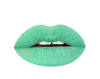 May include: Close-up of a pair of lips with bright green lipstick. The lipstick has a matte finish and is applied evenly.