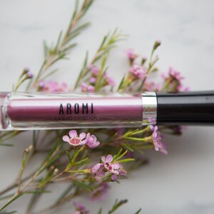 May include: A clear tube of pink liquid lipstick with a black cap. The label reads "AROMI LIQUID LIPSTICK".