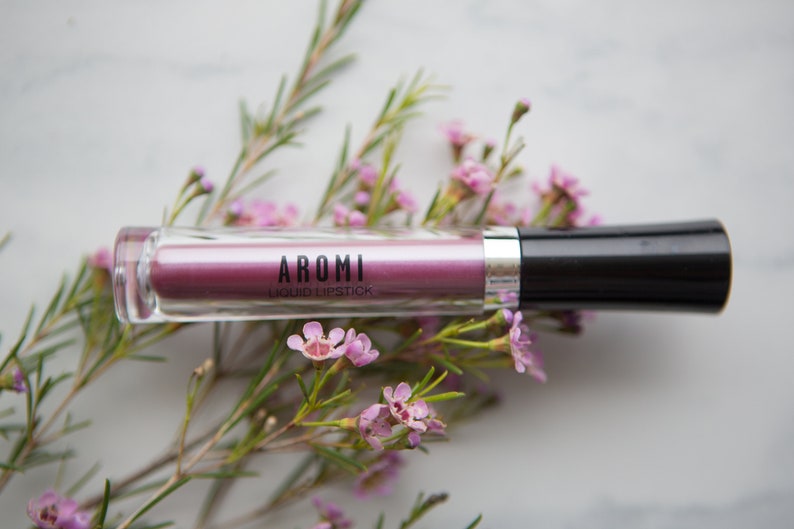 May include: A clear tube of pink liquid lipstick with a black cap. The label reads "AROMI LIQUID LIPSTICK".
