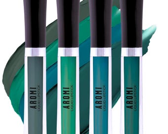 May include: Four tubes of AROMI liquid lipstick in shades of green and teal. Each tube has a black cap and silver band. The background features swatches of green and teal paint.