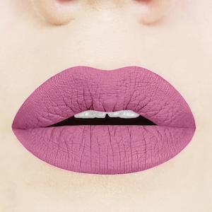 May include: Close-up of a person's lips wearing a matte, dusty rose-colored lipstick.