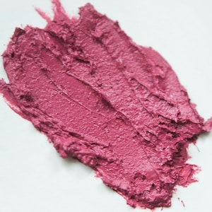 K&ouml;nnte beinhalten: Nahaufnahme eines rosa Lippenstift-Abstrichs auf einer wei&szlig;en Oberfl&auml;che. Der Lippenstift ist glatt und cremig mit einer leicht strukturierten Oberfl&auml;che.