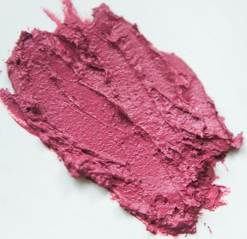 K&ouml;nnte beinhalten: Nahaufnahme eines rosa Lippenstift-Abstrichs auf einer wei&szlig;en Oberfl&auml;che. Der Lippenstift ist glatt und cremig mit einer leicht strukturierten Oberfl&auml;che.