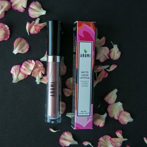 May include: Aromi Matte Liquid Lipstick in a mauve shade with a black and silver tube. The packaging features a pink and green floral design with the brand name "Aromi" and the product name "Matte Liquid Lipstick".