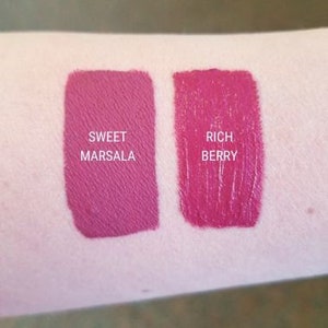 May include: Two swatches of liquid lipstick on a person's arm. The left swatch is a deep, cool-toned pink labeled "Sweet Marsala". The right swatch is a bright, warm-toned pink labeled "Rich Berry".
