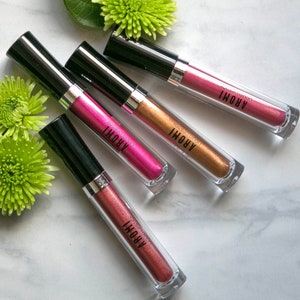 K&ouml;nnte beinhalten: Vier Tuben mit fl&uuml;ssigem Lippenstift in verschiedenen Metallic-Farbt&ouml;nen: Pink, Gold, Kupfer und Ros&eacute;gold. Jede Tube hat einen schwarzen Deckel und einen durchsichtigen K&ouml;rper, auf dem der Markenname "AROMI" aufgedruckt ist.