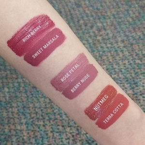 May include: Swatch of five different shades of lipstick on a person's arm. The shades are labeled "Rich Berry", "Sweet Marsala", "Rose Petal", "Berry Nude", and "Nutmeg Terra Cotta".