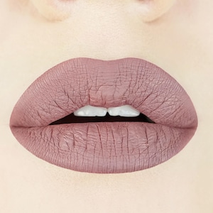 May include: Close-up of a person's lips wearing a mauve-coloured matte lipstick.