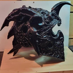 Puede incluir: Un casco negro, intrincadamente detallado, con cuernos curvos y una superficie texturizada. El casco presenta m&uacute;ltiples aberturas y un dise&ntilde;o amenazante, lo que sugiere un tema de fantas&iacute;a o g&oacute;tico. El color oscuro y los &aacute;ngulos agudos le dan una apariencia formidable.