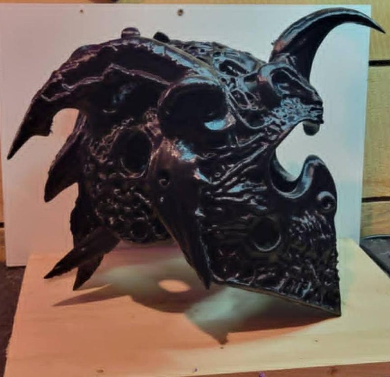 Puede incluir: Un casco negro, intrincadamente detallado, con cuernos curvos y una superficie texturizada. El casco presenta m&uacute;ltiples aberturas y un dise&ntilde;o amenazante, lo que sugiere un tema de fantas&iacute;a o g&oacute;tico. El color oscuro y los &aacute;ngulos agudos le dan una apariencia formidable.