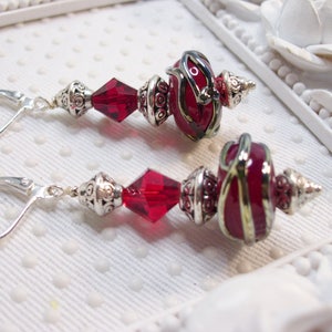 May include: A pair of red and silver dangle earrings with a red glass bead and a crystal bead. The earrings have a silver hook closure.