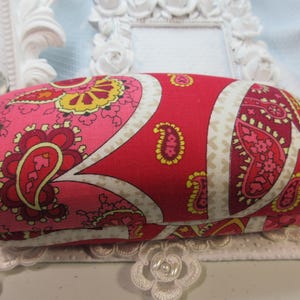 May include: A red, pink, and white paisley patterned glasses case.