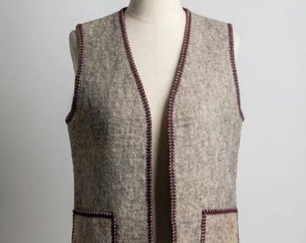Peut inclure: Un gilet en laine gris avec deux poches avant et un col en V. Le gilet est bordé d'une couture bordeaux foncé sur les bords et les poches. Le gilet est présenté sur un mannequin.