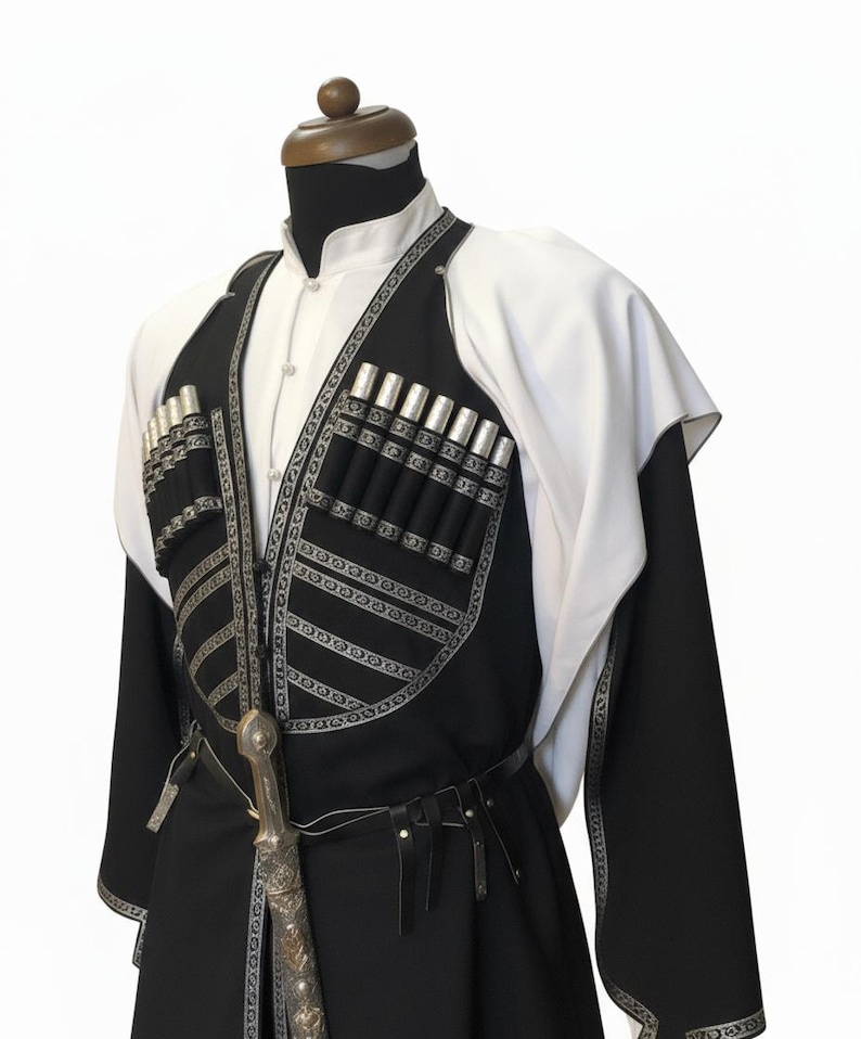May include: A traditional black and white outfit with silver detailing, presented on a mannequin. The outfit features a long coat, a vest with cartridge holders, and a decorative dagger. A white shirt and cape complete the ensemble.