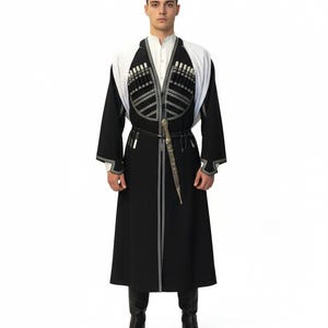 May include: A traditional black Chokha coat with white detailing and silver embroidery. The coat has a white collar and shoulder detail, and is worn with black boots. A dagger is attached to the belt.