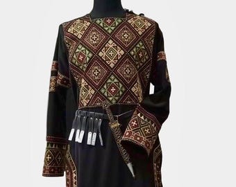 Puede incluir: Túnica negra con intrincados bordados geométricos en tonos marrón, rojo y verde. La prenda de manga larga presenta un cinturón decorativo y una daga. La túnica se exhibe en un maniquí.
