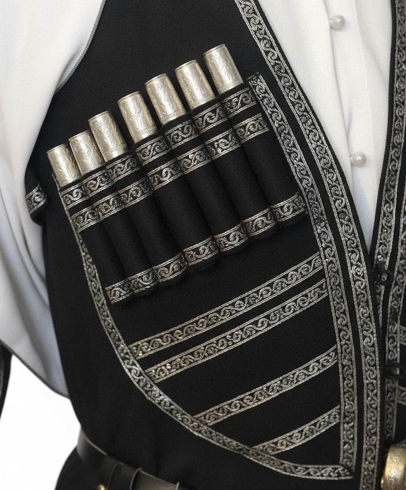 May include: Close-up of a black vest with silver decorative trim and seven silver-topped cylindrical holders. The vest is worn over a white shirt. The vest has horizontal silver stripes and a decorative silver border.