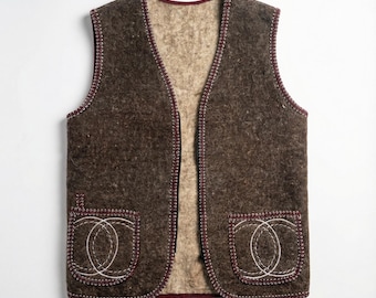 Peut inclure: Un gilet en laine marron avec un intérieur crème et deux poches avant. Le gilet présente un motif décoratif blanc cousu sur les poches et les bords, avec une bordure bordeaux. Le gilet sans manches a un col en V.