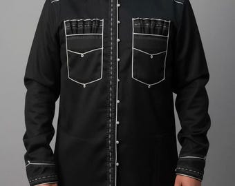 Puede incluir: Camisa negra de manga larga con detalles de costura blancos. La camisa presenta un cuello mandarín, cierre de botones en la parte delantera y dos bolsillos en el pecho con adornos decorativos. Los puños y las costuras también están acentuados con costuras blancas.